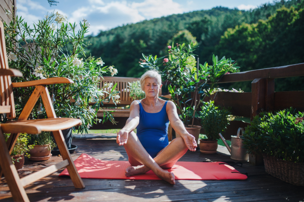 A senior woman sitting outdoors on a terrace in summer, doing yoga exercise. Copy space.