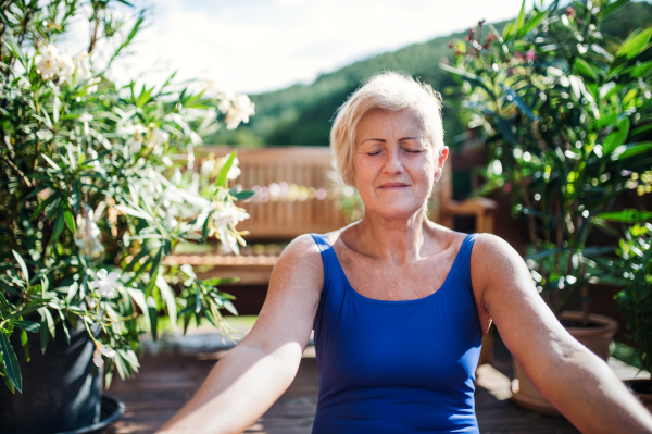 A senior woman sitting outdoors on a terrace in summer, doing yoga exercise. Copy space.