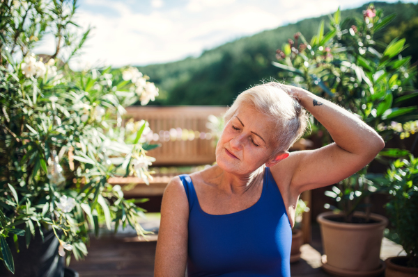 A senior woman standing outdoors on a terrace in summer, doing stretching. Copy space.