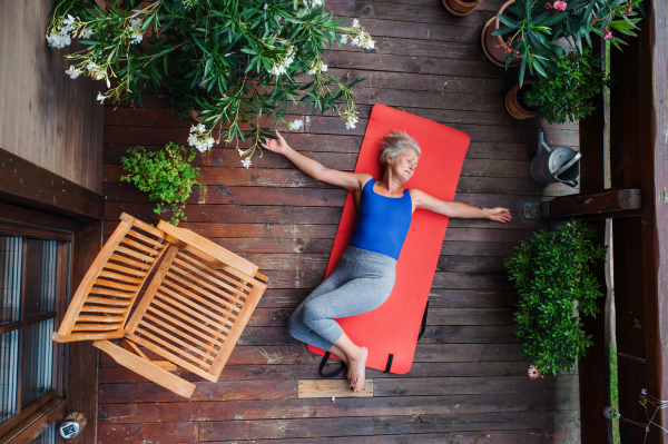 A top view of senior woman outdoors on a terrace in summer, doing exercise on mat.