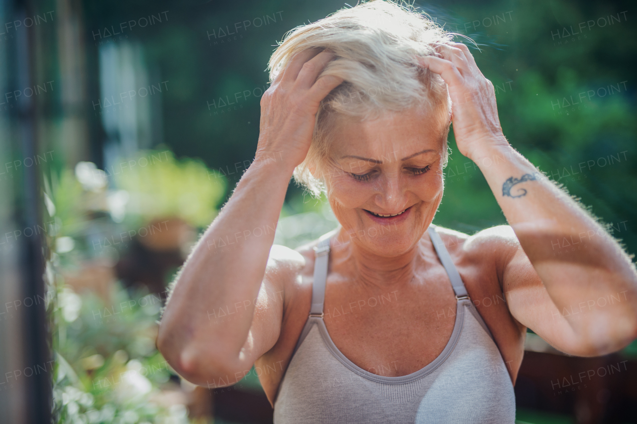 A front view of senior woman with sports bra standing outdoors on a terrace in summer.