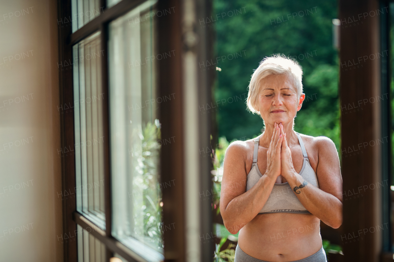 A senior woman with sports bra standing outdoors on a terrace in summer, doing yoga.