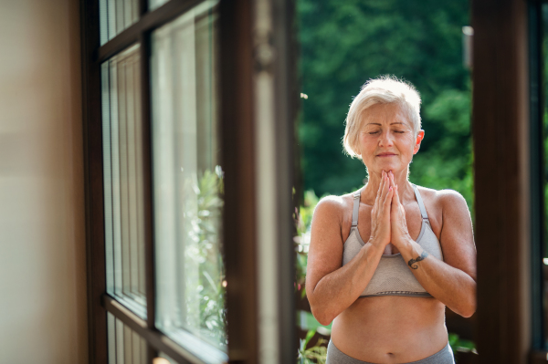 A senior woman with sports bra standing outdoors on a terrace in summer, doing yoga.