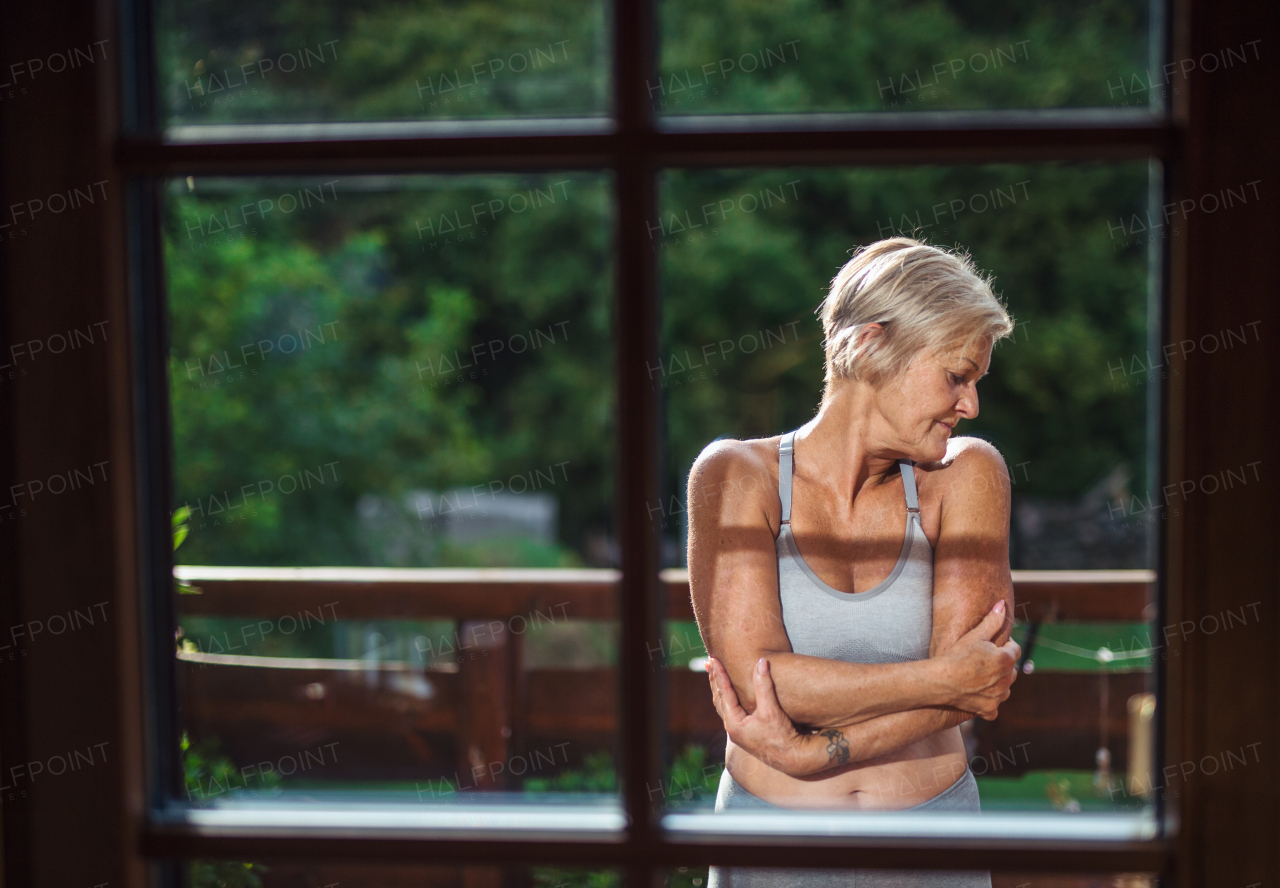 A front view of senior woman with sports bra standing outdoors on a terrace in summer.