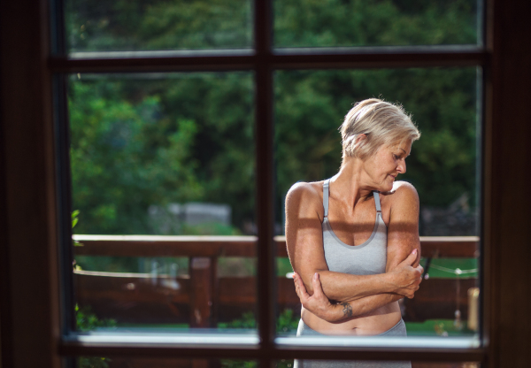 A front view of senior woman with sports bra standing outdoors on a terrace in summer.