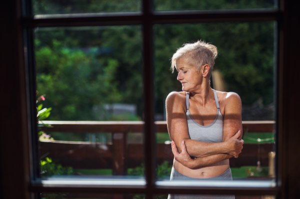 A front view of senior woman with sports bra standing outdoors on a terrace in summer.