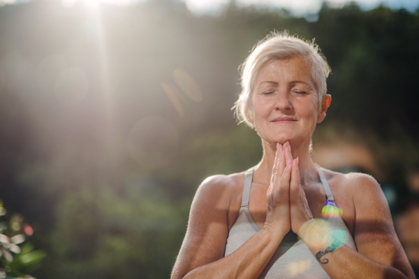 A senior woman with sports bra standing outdoors on a terrace in summer, doing yoga.