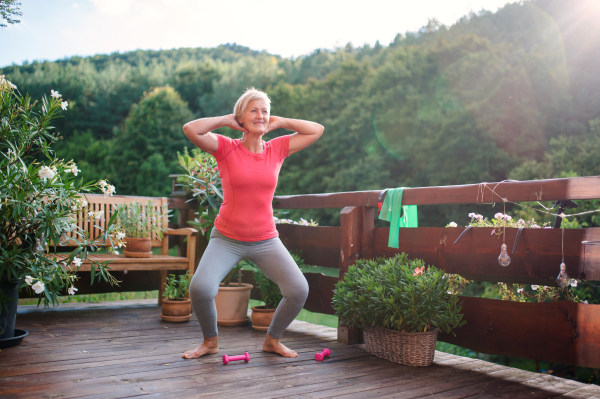 A senior woman standing outdoors on a terrace in summer, doing exercise. Copy space.