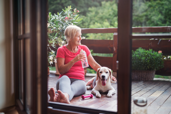 A senior woman with dog outdoors on a terrace in summer, resting after exercise.