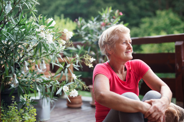 A senior woman sitting outdoors on a terrace in summer, resting after exercise.