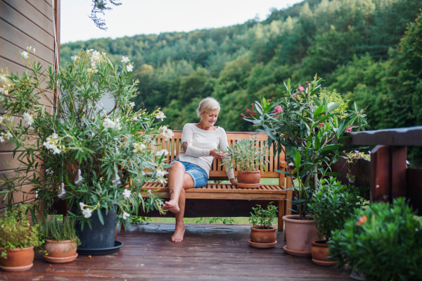 A happy senior woman sitting outdoors on a terrace in summer, resting.