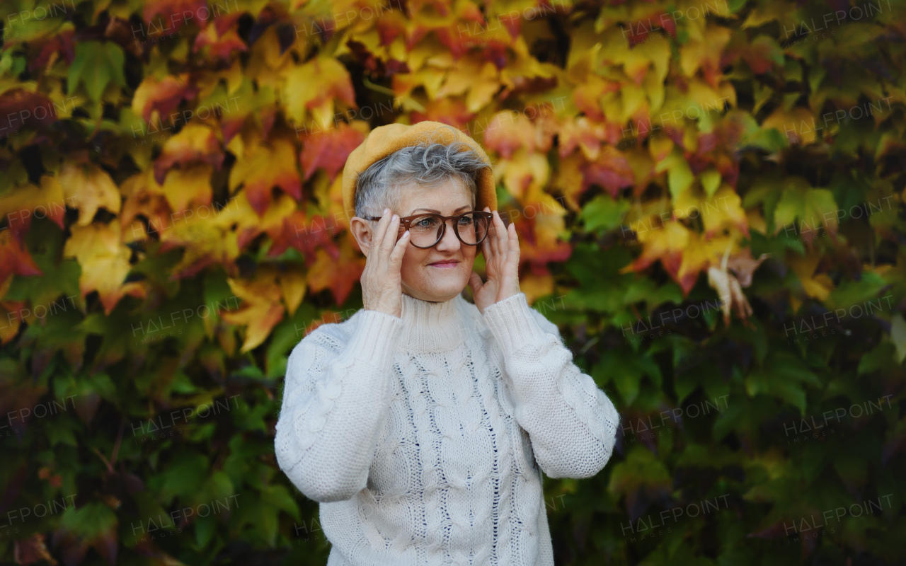 Portrait of senior woman standing outdoors against colorful natural autumn background.