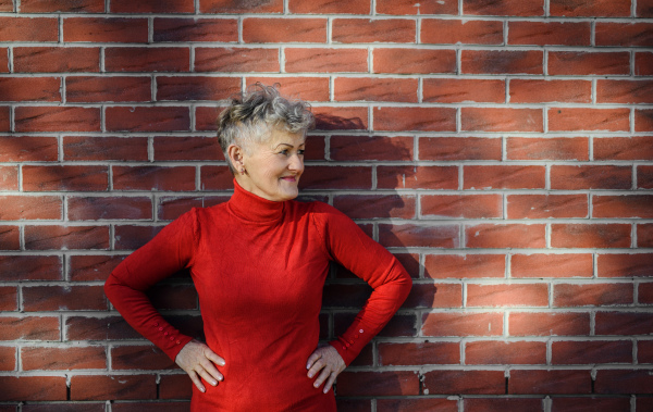 Portrait of senior woman standing outdoors against brick wall background. Copy space.