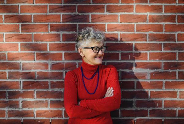 Portrait of senior woman standing outdoors against brick wall background. Copy space.