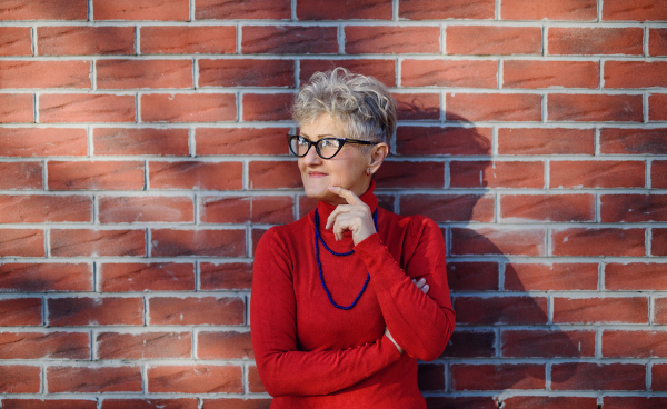 Portrait of senior woman standing outdoors against brick wall background. Copy space.