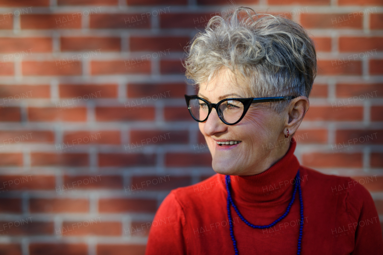 Portrait of senior woman standing outdoors against brick wall background. Copy space.