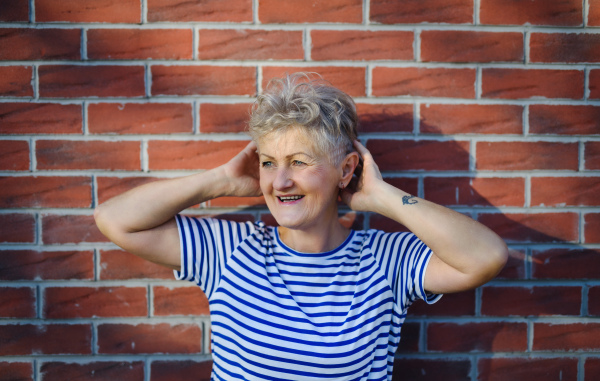 Portrait of senior woman standing outdoors against brick wall background, relaxing.