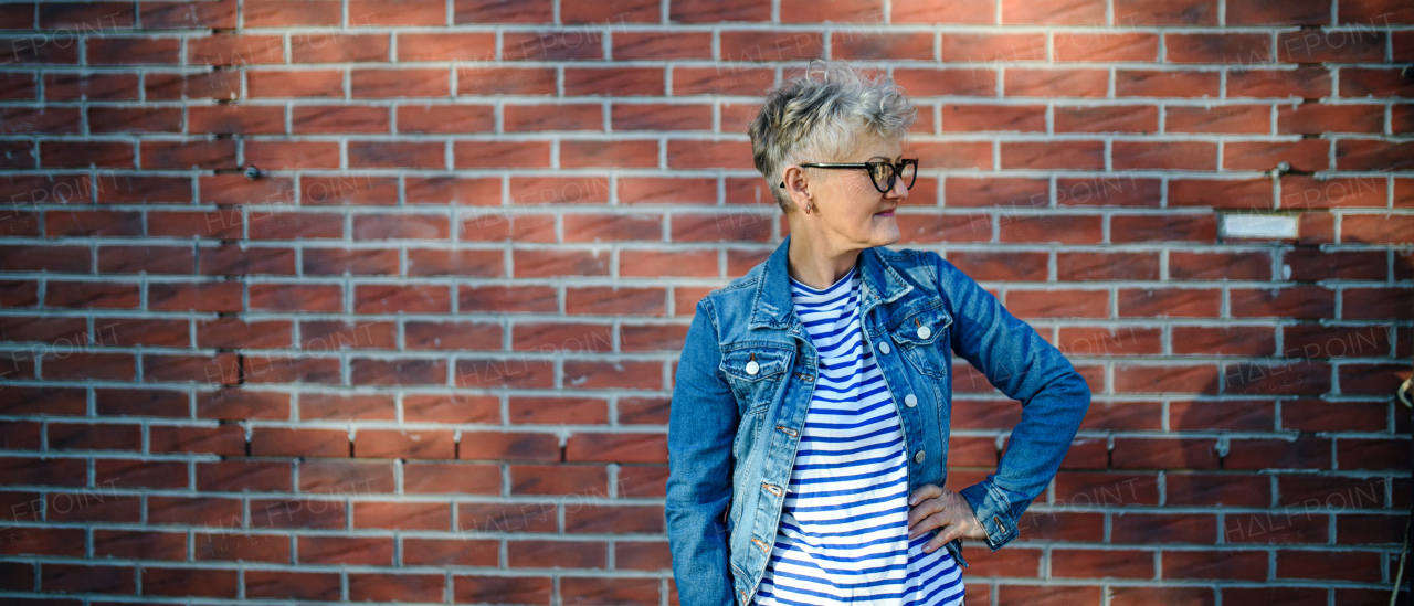 Portrait of senior woman standing outdoors against brick wall background. Copy space.