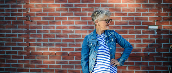 Portrait of senior woman standing outdoors against brick wall background. Copy space.