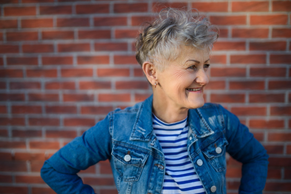 Portrait of senior woman standing outdoors against brick wall background. Copy space.