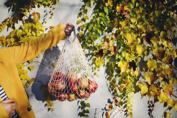 An unrecognizable woman standing outdoors holding shopping in reusable bag, sustainable lifestyle.