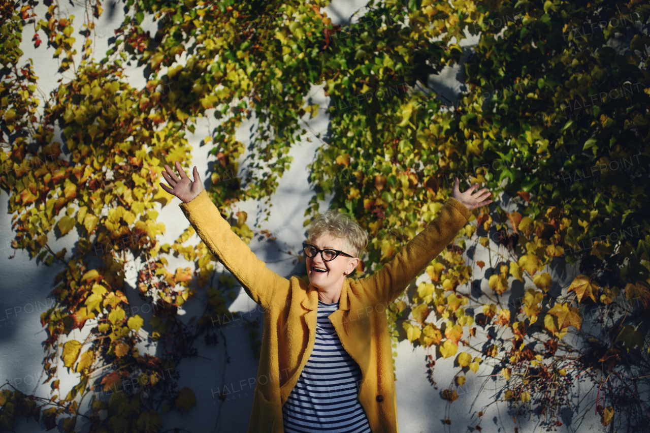 Portrait of senior woman standing outdoors against colorful natural autumn background, stretching arms.