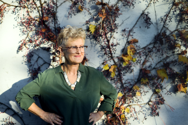 Portrait of senior woman standing outdoors against wall in town, hands on hips.