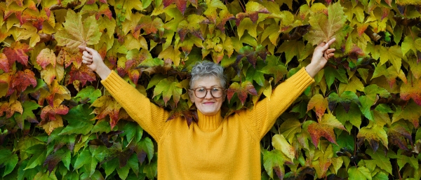 Portrait of senior woman standing outdoors against colorful natural autumn background, stretching arms.