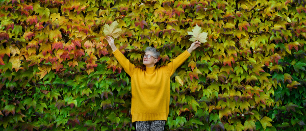 Portrait of senior woman standing outdoors against colorful natural autumn background, stretching arms.