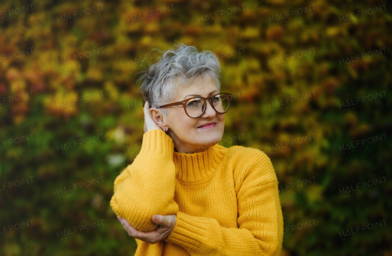 Portrait of senior woman standing outdoors against colorful natural autumn background, resting.