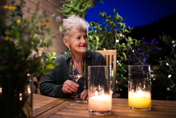 Portrait of happy senior woman in the evening on terrace, drinking wine.