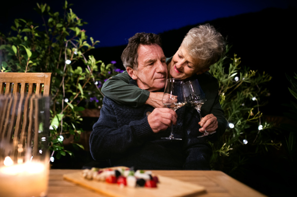 Portrait of senior couple in the evening on terrace, drinking wine.