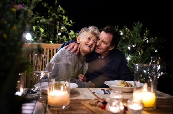 Portrait of happy senior couple having dinner in the evening on terrace.