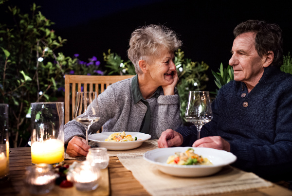 Happy senior couple having dinner in the evening on terrace, drinking wine.