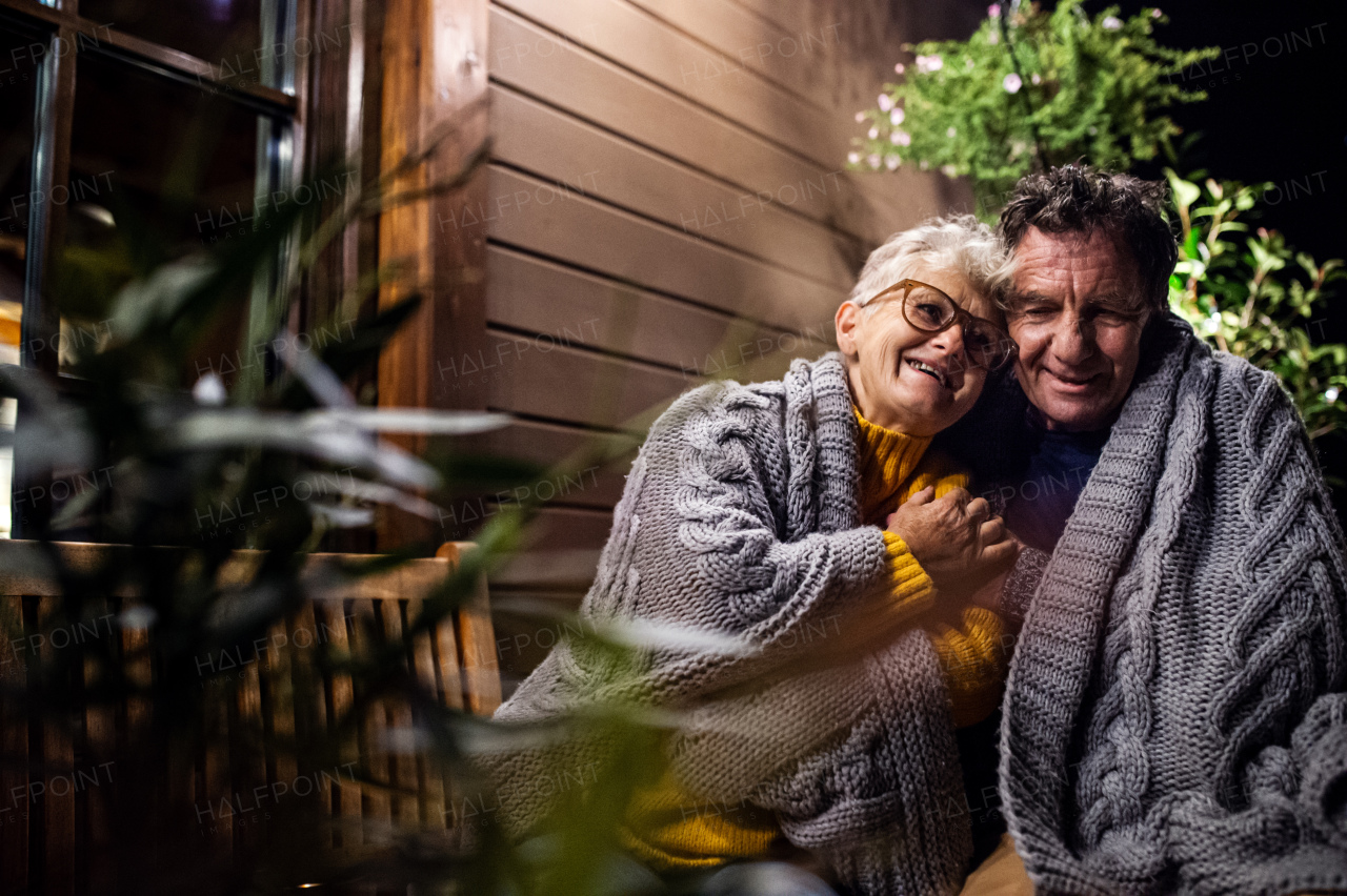 Close-up portrait of senior couple sitting in the evening on terrace, hugging.