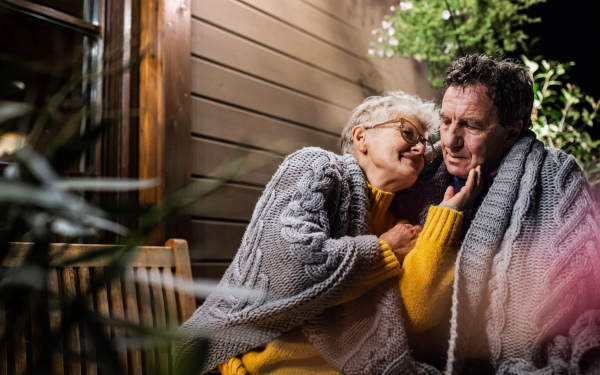 Close-up portrait of senior couple sitting in the evening on terrace, hugging.