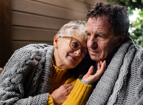 Close-up portrait of senior couple sitting in the evening on terrace, hugging.