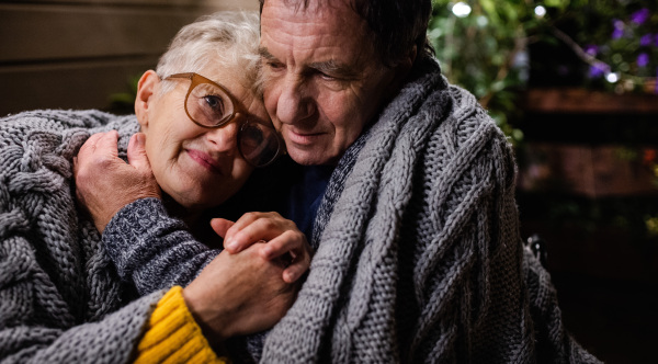 Close-up portrait of senior couple sitting in the evening on terrace, hugging.