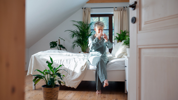 A happy senior woman on bed at home, getting up and drinking water.