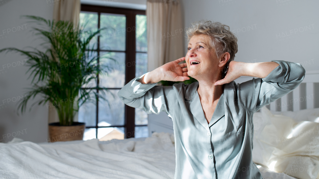 A cheerful senior woman in bed at home getting up in the morning, stretching.