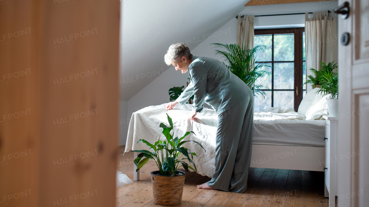 Happy senior woman in bed at home getting up in the morning, making a bed.