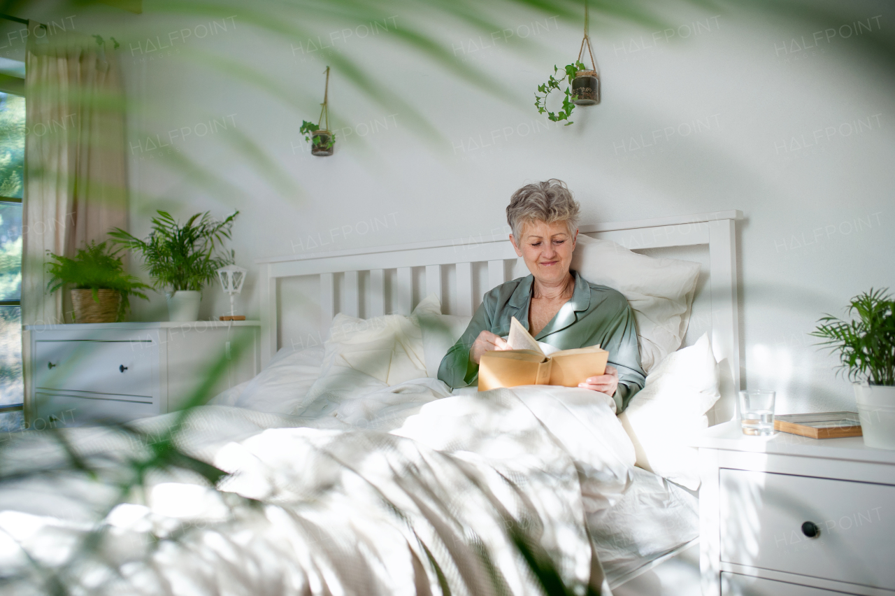 Happy senior woman reading a book in bed at home.