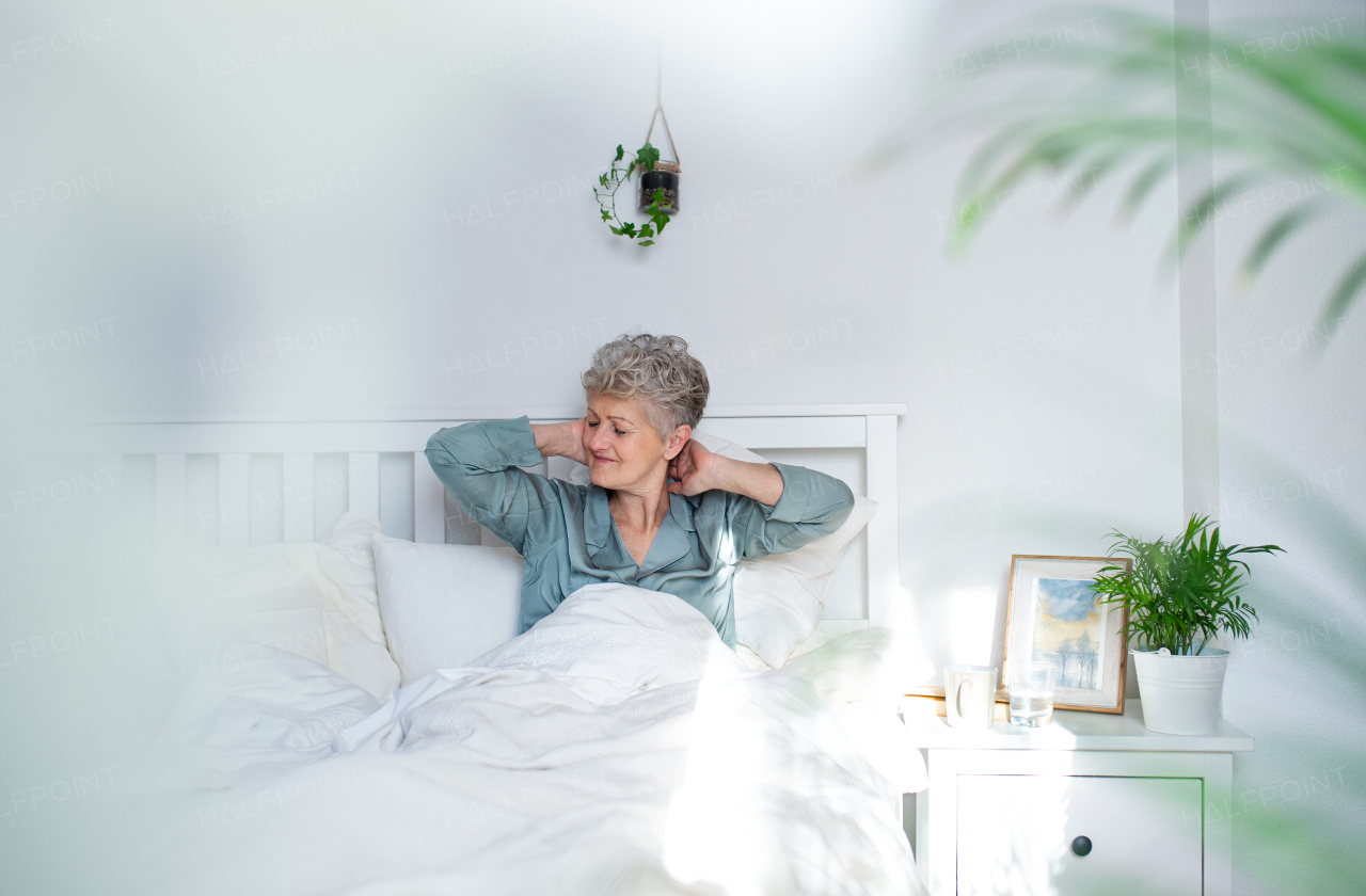 Happy senior woman in bed at home getting up in the morning, stretching.