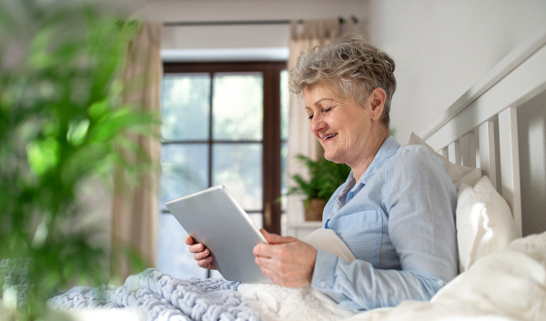 Portrait of happy senior woman using tablet in bed at home.