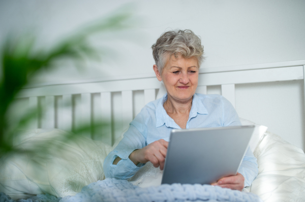 Portrait of happy senior woman using tablet in bed at home.