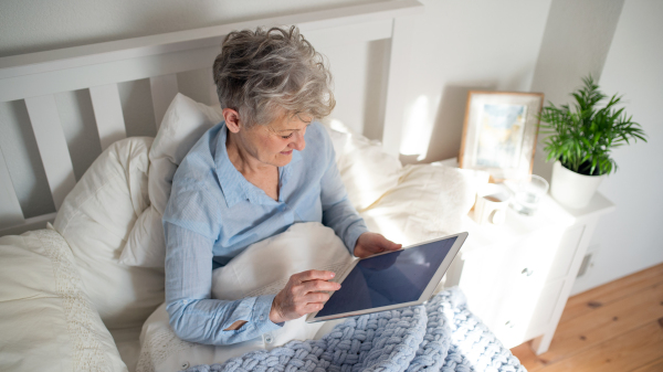 Portrait of happy senior woman using tablet in bed at home.