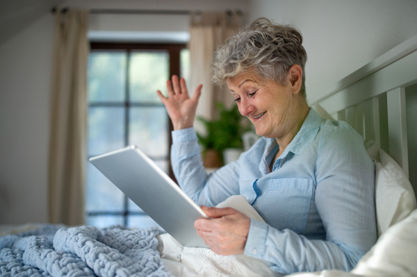 A happy senior woman using tablet in bed at home, video call concept.