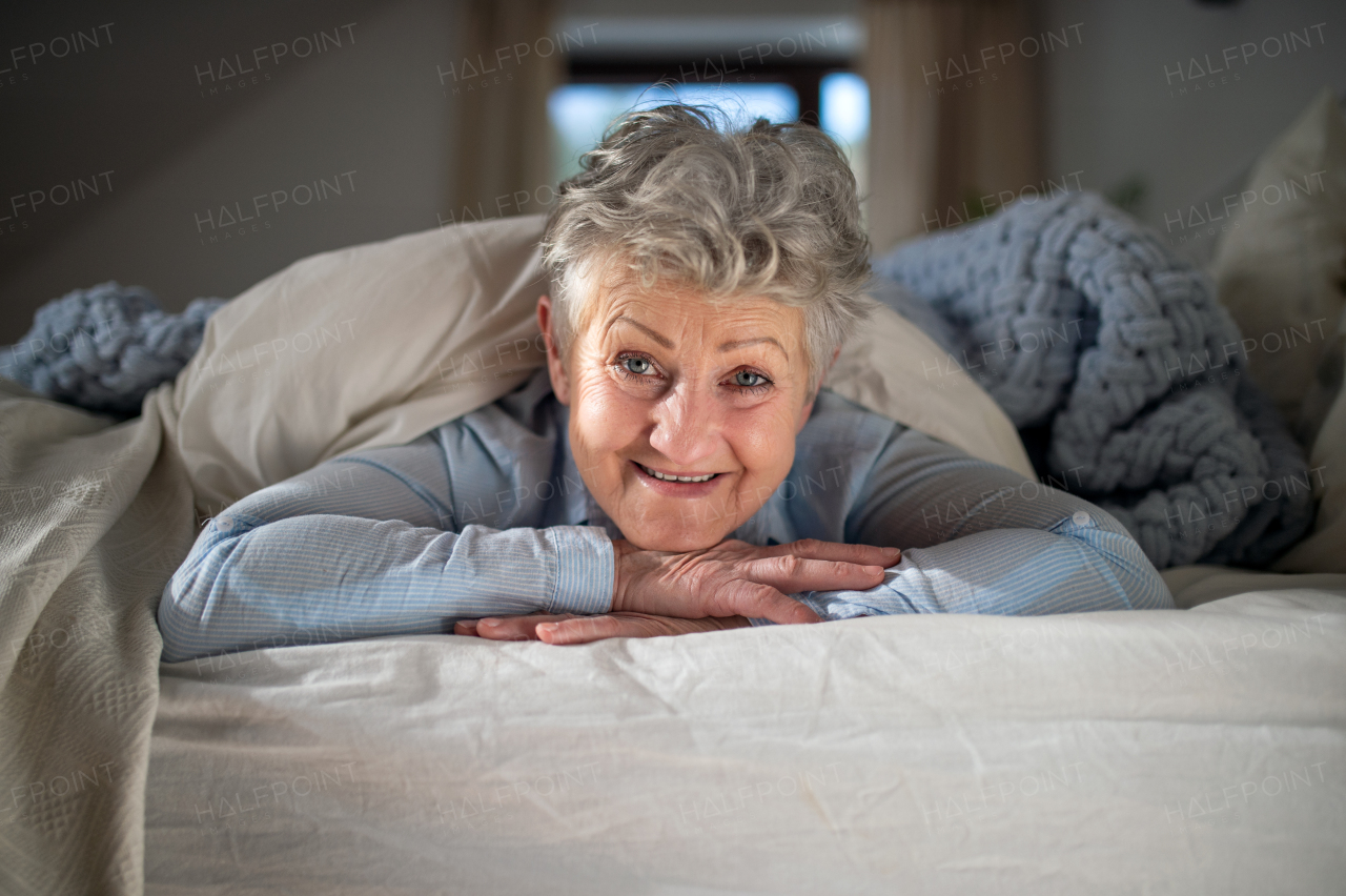 Portrait of happy senior woman in bed at home, looking at camera.