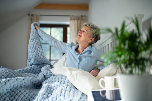 Happy senior woman in bed at home getting up in the morning, stretching.