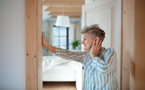 Side view of senior woman standing by door at home, getting up in the morning.